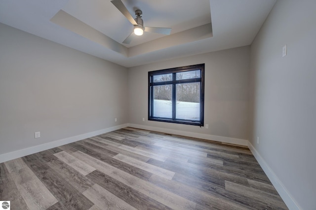 empty room featuring ceiling fan, a raised ceiling, baseboards, and wood finished floors