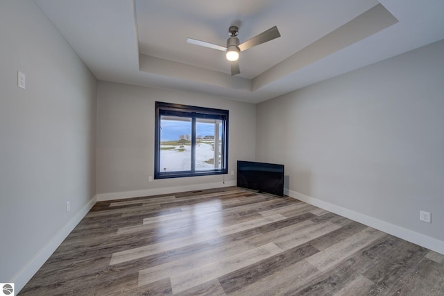 unfurnished living room featuring a raised ceiling, wood finished floors, baseboards, and ceiling fan