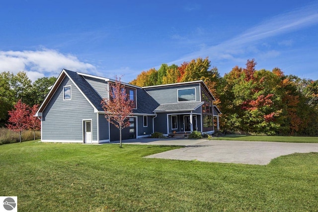 rear view of house with concrete driveway, a lawn, a garage, and a shingled roof