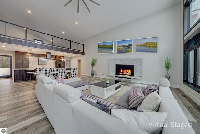 living room featuring light wood-type flooring, high vaulted ceiling, recessed lighting, a premium fireplace, and baseboards