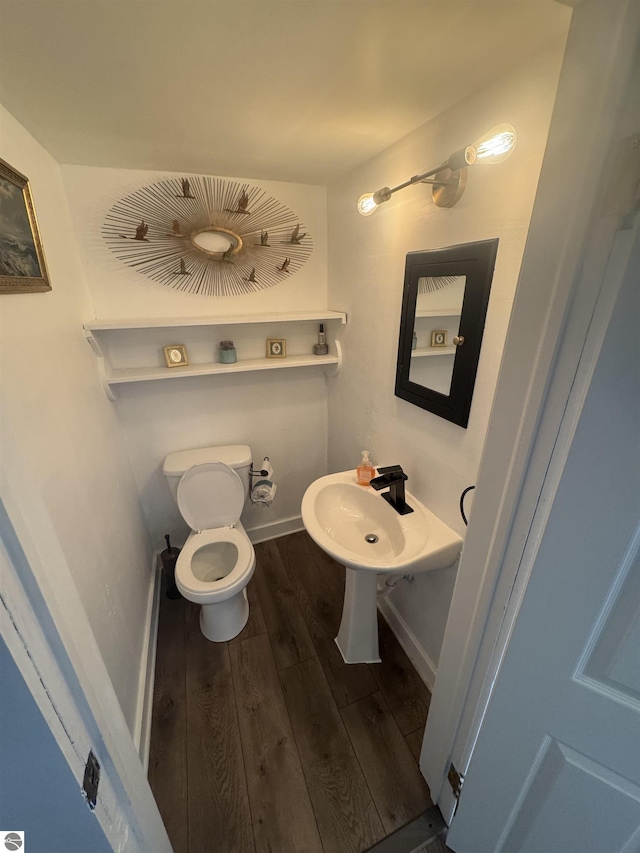 half bath with baseboards, a sink, toilet, and wood finished floors