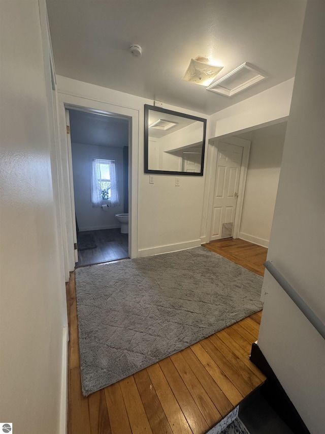 corridor featuring attic access, baseboards, and hardwood / wood-style floors