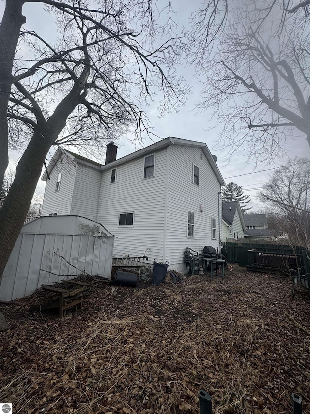 back of house with a chimney and fence