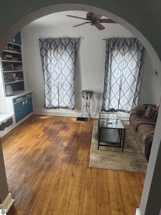 unfurnished living room with wood-type flooring, built in features, arched walkways, and a ceiling fan