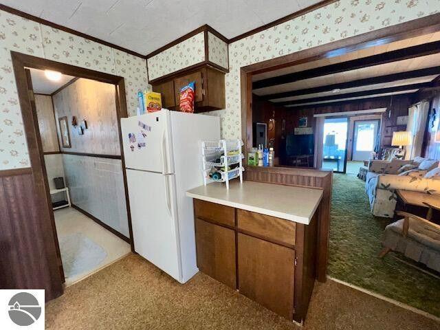 kitchen with wallpapered walls, ornamental molding, open floor plan, freestanding refrigerator, and light countertops