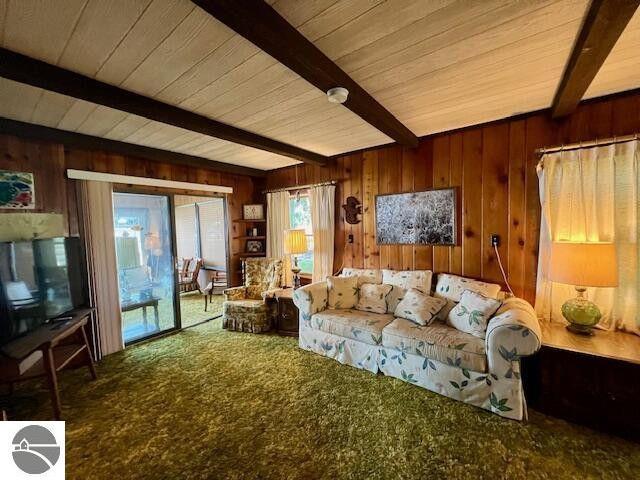 living area with wood walls, beam ceiling, and carpet flooring