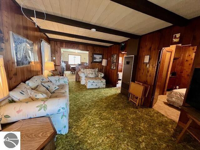 living room featuring carpet floors, wooden walls, and beam ceiling