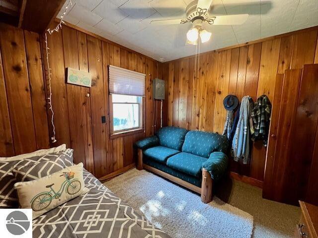 carpeted living room featuring a ceiling fan and wooden walls