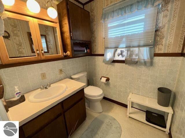 bathroom featuring tile walls, vanity, toilet, and wallpapered walls