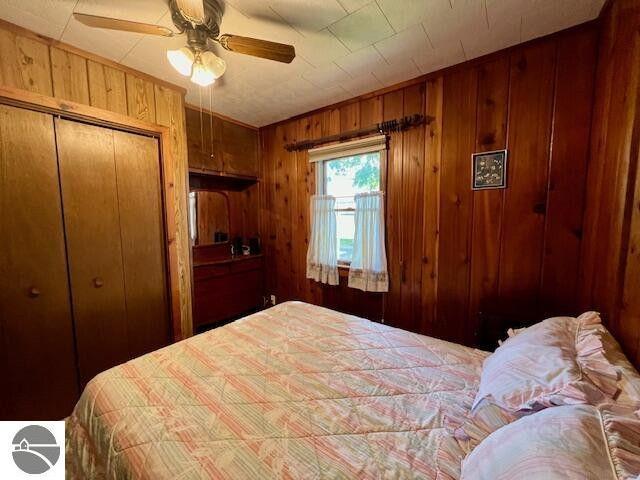 bedroom featuring a ceiling fan, a closet, and wooden walls