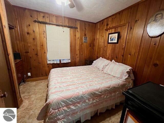 bedroom featuring light carpet, ceiling fan, and wooden walls