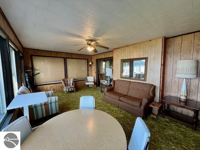 carpeted living area featuring a ceiling fan and wooden walls