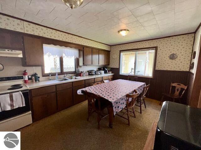 kitchen with white electric range oven, a wainscoted wall, under cabinet range hood, and wallpapered walls