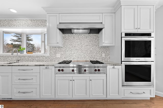 kitchen with tasteful backsplash, wall chimney exhaust hood, appliances with stainless steel finishes, light stone countertops, and a sink