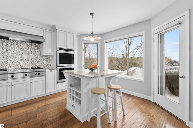 kitchen with a breakfast bar area, light wood-style flooring, stainless steel appliances, decorative backsplash, and wall chimney exhaust hood