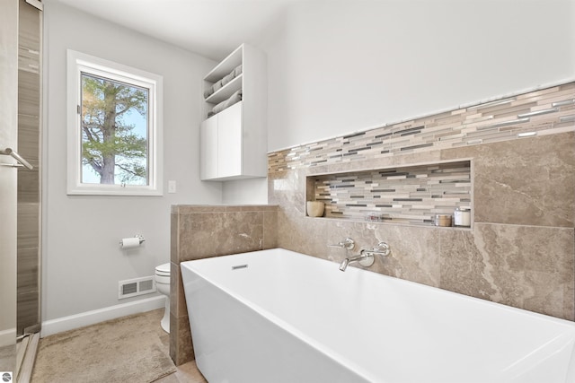 full bathroom with baseboards, visible vents, a freestanding bath, and toilet