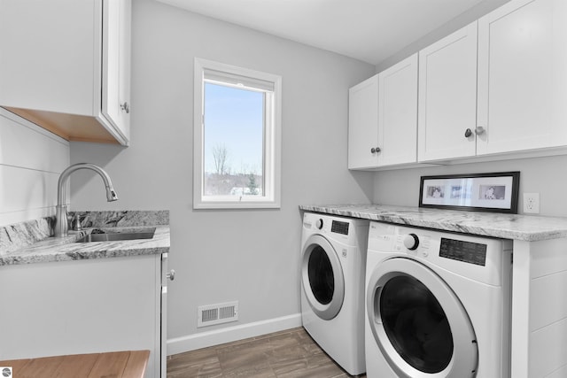 washroom featuring a sink, visible vents, baseboards, cabinet space, and washer and clothes dryer