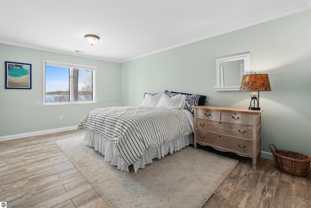 bedroom featuring ornamental molding, baseboards, visible vents, and light wood finished floors