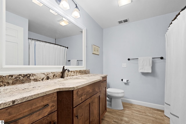 bathroom featuring visible vents, toilet, vanity, wood finished floors, and baseboards