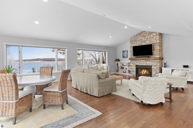 living room featuring recessed lighting, a water view, vaulted ceiling, a stone fireplace, and hardwood / wood-style flooring