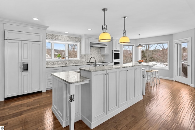 kitchen with dark wood finished floors, a sink, a center island with sink, and wall chimney exhaust hood