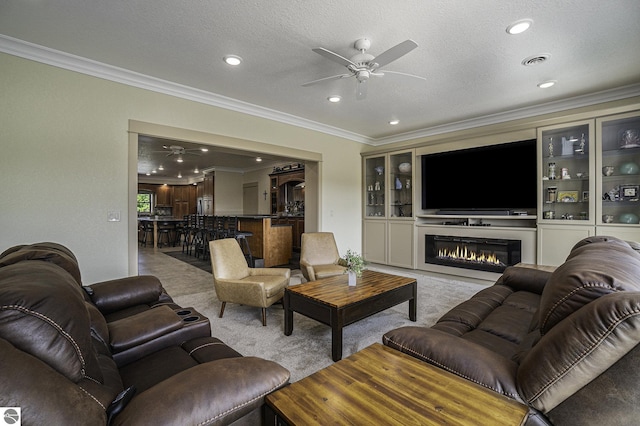 carpeted living room with visible vents, a glass covered fireplace, a ceiling fan, and ornamental molding