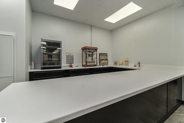 kitchen with a paneled ceiling, wine cooler, light countertops, and dark cabinetry