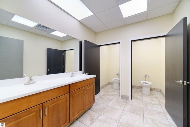 full bath featuring a drop ceiling, a sink, toilet, and double vanity