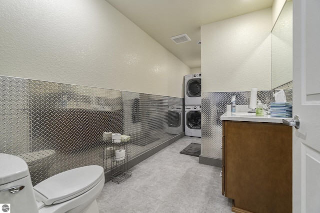 bathroom with visible vents, stacked washer / dryer, toilet, a wainscoted wall, and vanity