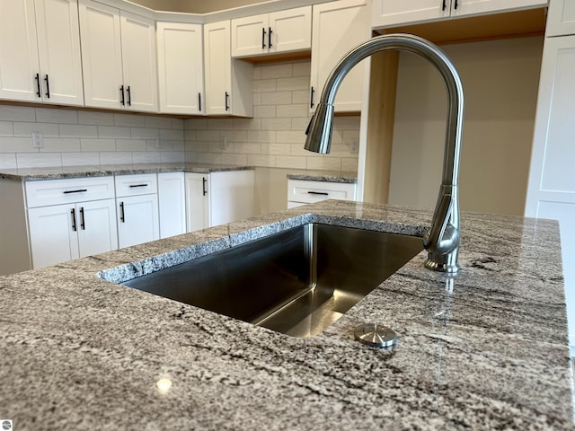 kitchen with a sink, white cabinetry, light stone counters, and backsplash