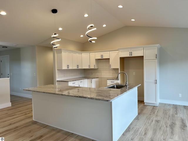 kitchen featuring vaulted ceiling, light wood-type flooring, a sink, and white cabinetry