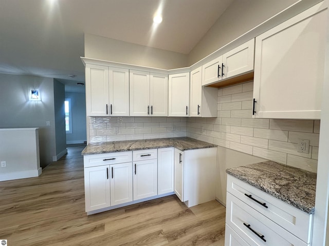 kitchen with white cabinets, light wood finished floors, stone countertops, and tasteful backsplash