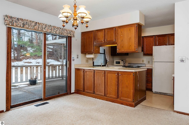 kitchen with brown cabinetry, visible vents, light countertops, and freestanding refrigerator