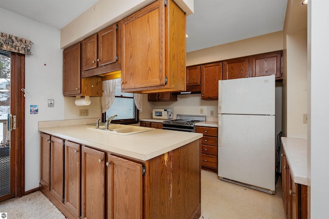 kitchen featuring brown cabinetry, freestanding refrigerator, light countertops, stainless steel range oven, and a sink