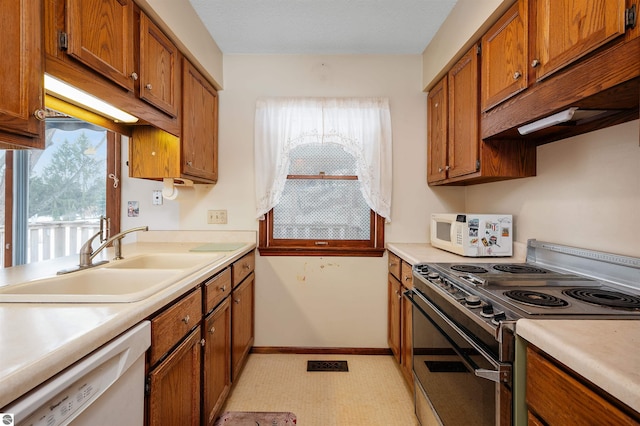 kitchen featuring light countertops, white appliances, a sink, and brown cabinets