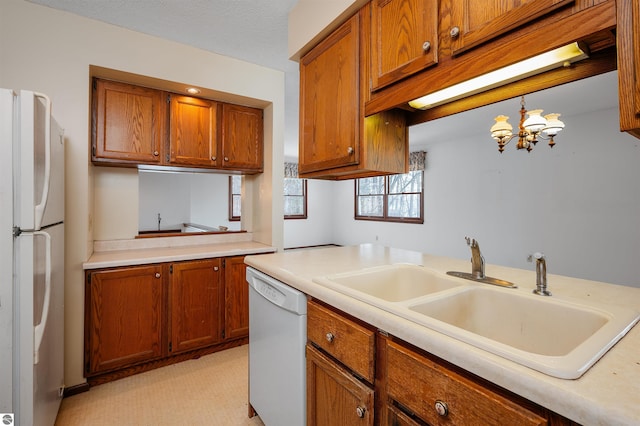 kitchen featuring brown cabinets, a notable chandelier, light countertops, a sink, and white appliances