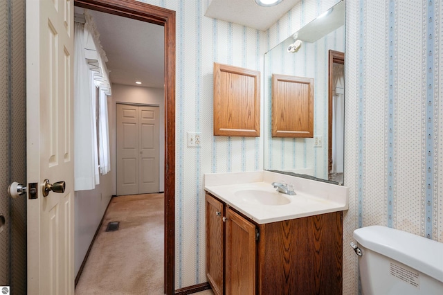 bathroom with visible vents, vanity, toilet, and wallpapered walls