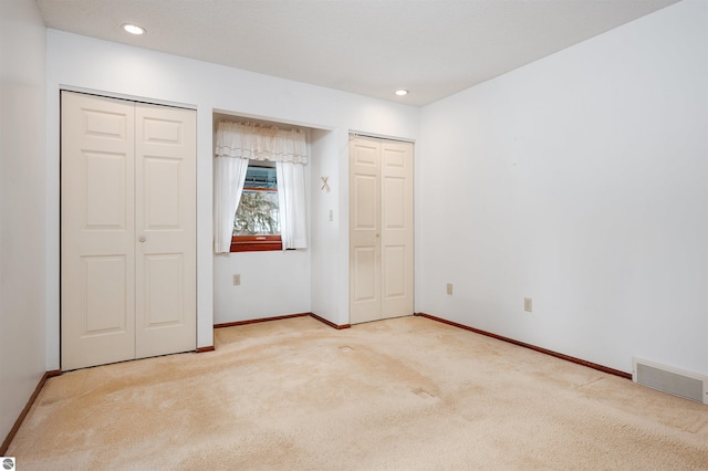 unfurnished bedroom featuring multiple closets, carpet, visible vents, and baseboards