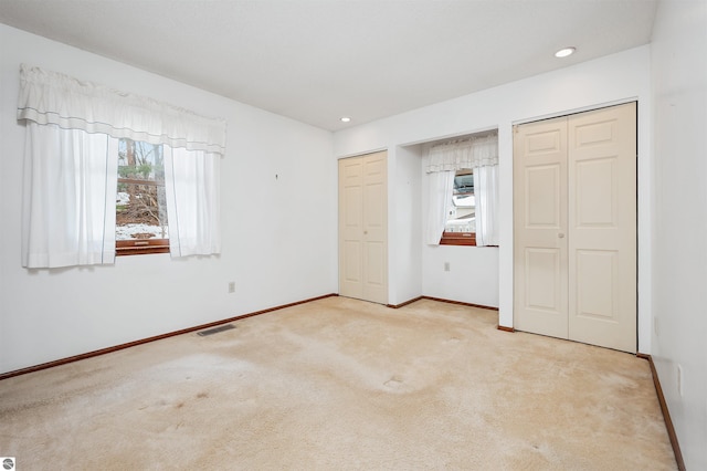 unfurnished bedroom with carpet floors, visible vents, multiple windows, and two closets