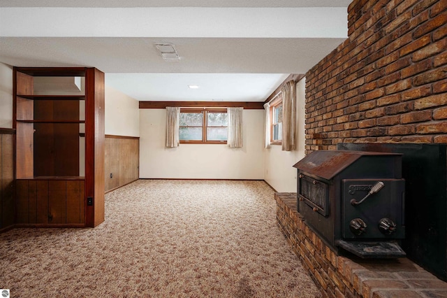 unfurnished living room with a wainscoted wall, visible vents, a wood stove, carpet flooring, and wood walls