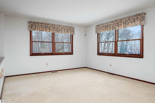 carpeted empty room with baseboards, visible vents, and a textured ceiling