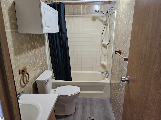 bathroom with toilet, wood finished floors, vanity, tile walls, and shower / bath combo