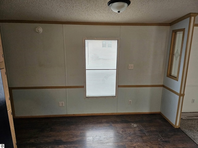 empty room with a wealth of natural light, a textured ceiling, ornamental molding, and dark wood-type flooring