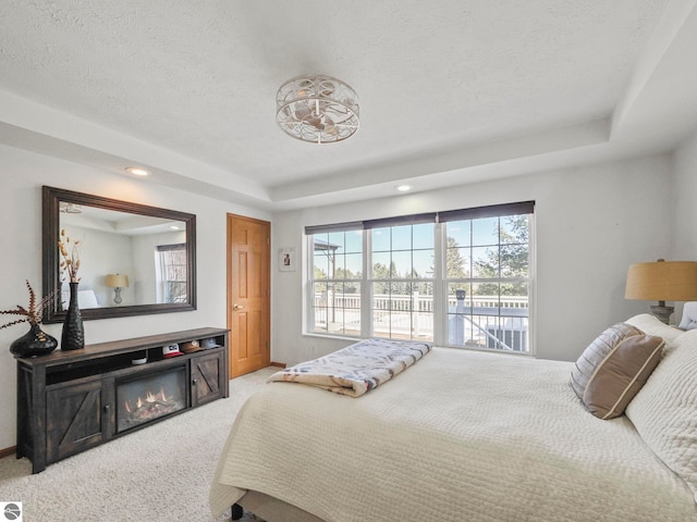 bedroom with a textured ceiling, a tray ceiling, carpet flooring, and baseboards