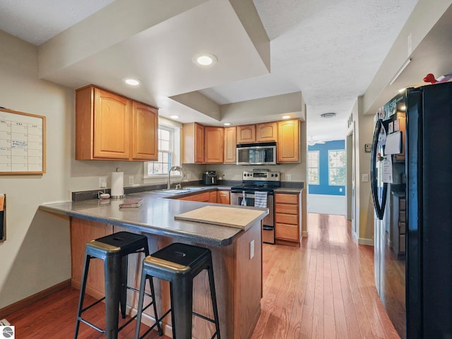 kitchen with stainless steel appliances, a peninsula, a sink, and light wood-style floors