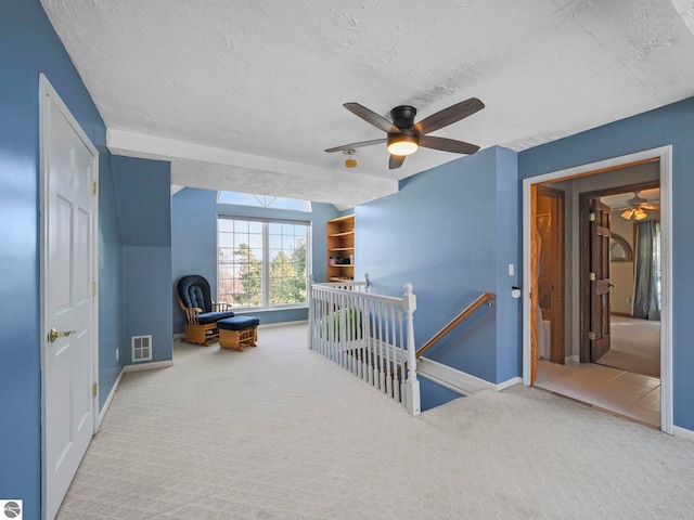 hall with a textured ceiling, carpet, an upstairs landing, and visible vents