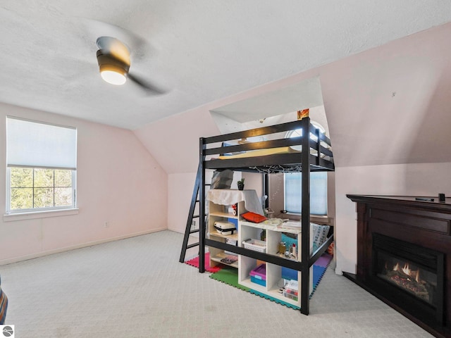 bedroom featuring a ceiling fan, a glass covered fireplace, vaulted ceiling, a textured ceiling, and carpet flooring