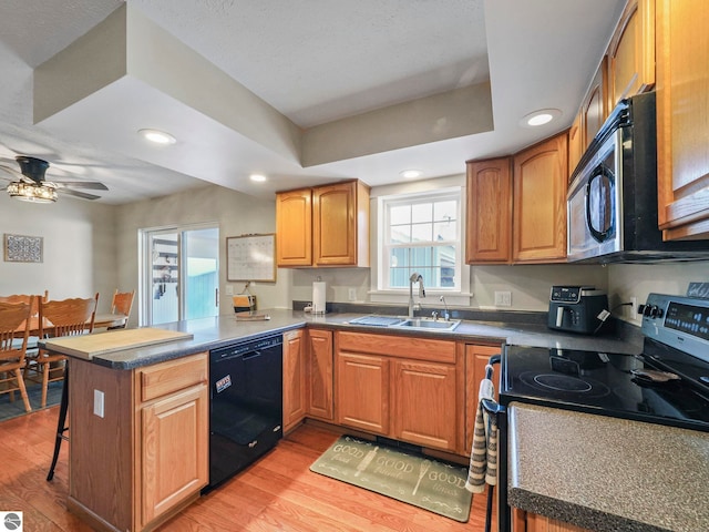 kitchen featuring black dishwasher, a peninsula, a tray ceiling, stainless steel range with electric stovetop, and a sink