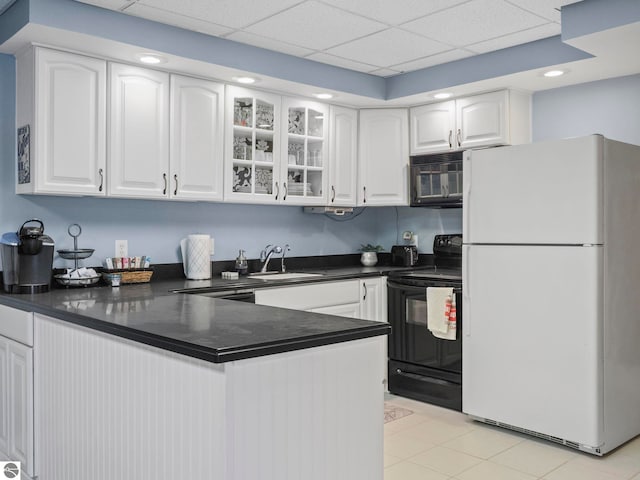 kitchen with white cabinets, dark countertops, a peninsula, black appliances, and a sink