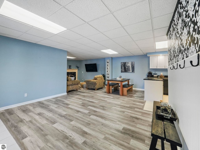 living area with light wood-style flooring, a fireplace, baseboards, and a drop ceiling